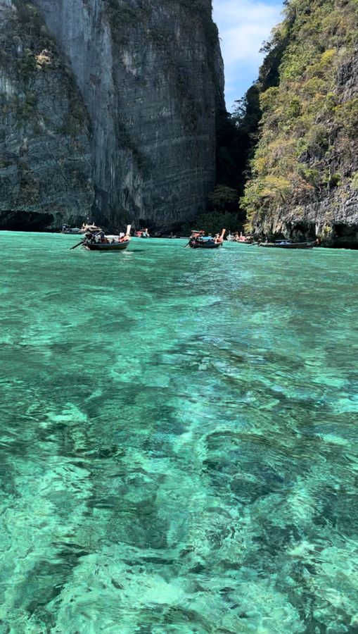 Longtail boats in clear turquoise water under tall cliffs