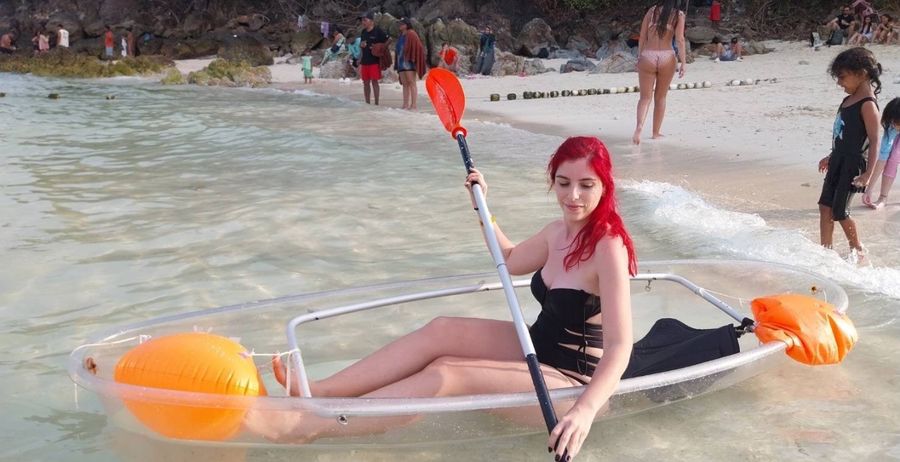 Guest paddling a transparent kayak by the beach