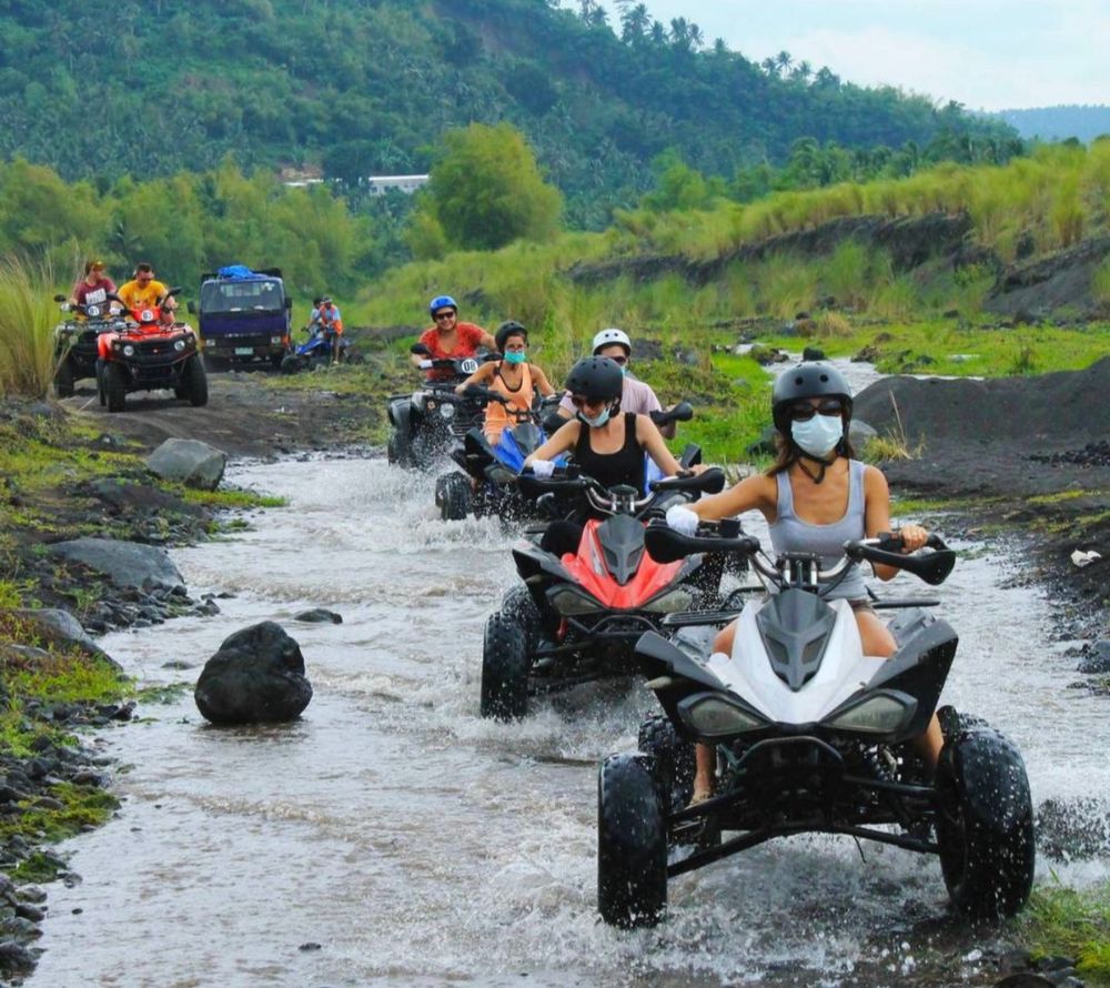 Line of guests riding ATVs through a shallow stream